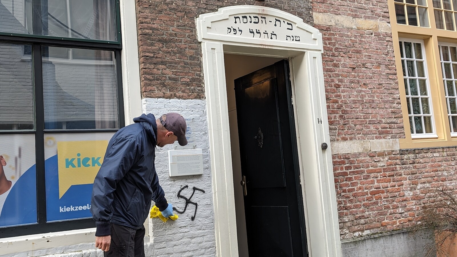 Een man poetst een hakenkruis van de gevel van een synagoge